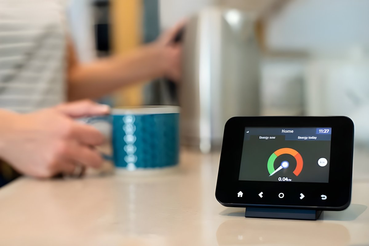 A smart meter in-home display showing energy usage on a kitchen counter next to a person holding a mug.