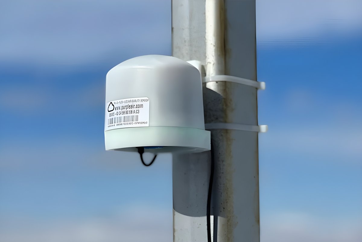 A PurpleAir air quality sensor mounted to a metal utility pole with zip ties against a blue sky.