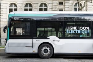 Side profile of an electric RATP bus with "Ligne 100% Électrique" signage parked on a cobblestone street in front of a building.