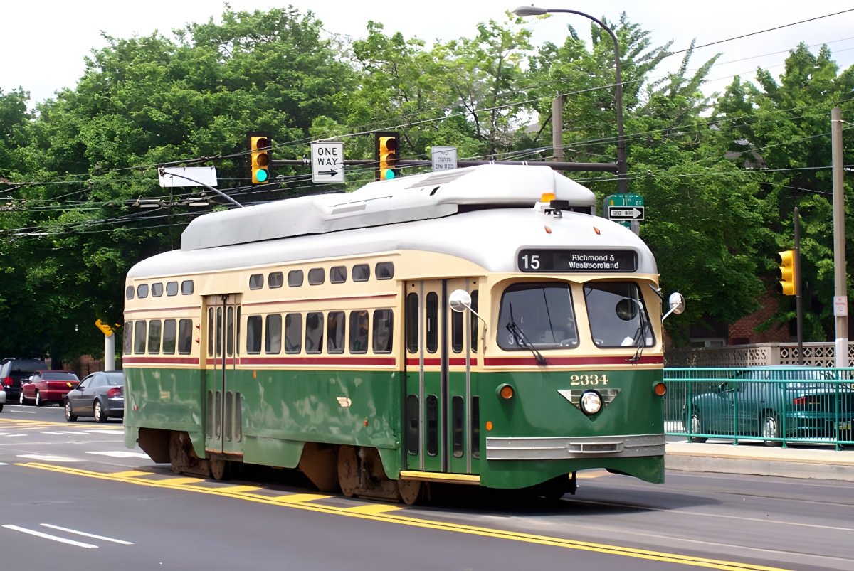 Green and cream SEPTA Route 15 trolley traveling on a Philadelphia city street with traffic lights and trees.