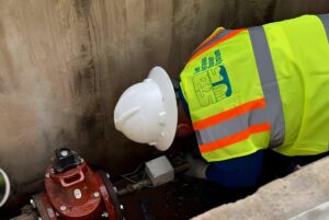 A San Antonio Water System worker in a hard hat and safety vest installs a smart water meter in an underground utility vault.