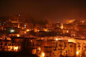 Nighttime view of San Giovanni in Fiore with warm orange street lighting illuminating the hillside buildings.