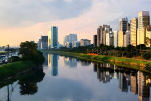 Skyline of São Paulo buildings reflecting in the Pinheiros River at sunset.