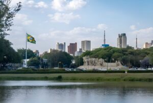 The Monument to the Bandeiras and a Brazilian flag in front of the São Paulo skyline and Ibirapuera Park lake.