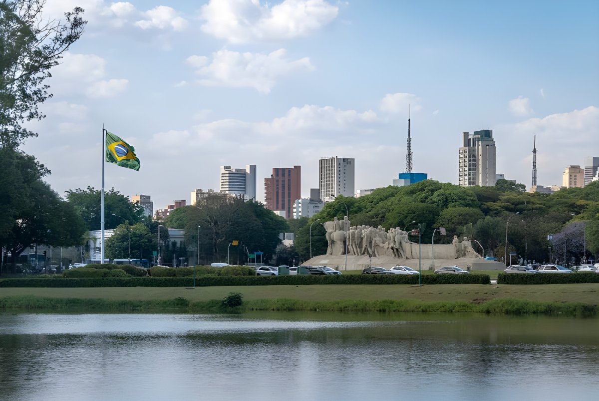 The Monument to the Bandeiras and a Brazilian flag in front of the São Paulo skyline and Ibirapuera Park lake.