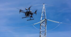 A DJI Matrice drone flying near a National Grid high-voltage electricity pylon and power lines against a blue sky.