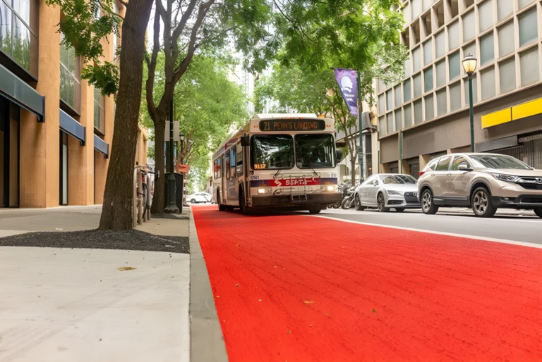 A SEPTA bus driving on a red-painted dedicated bus lane on a tree-lined Philadelphia city street.