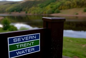 Severn Trent Water signage on a wooden post overlooking a reservoir and forested hills.