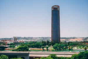The Seville Tower skyscraper overlooking the Guadalquivir River and city skyline under a clear blue sky.