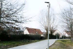Upciti smart sensors mounted on a street lamp post along a paved path in a rural residential area.