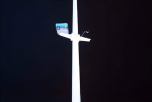 Low-angle view of a white utility pole with a mounted smart traffic camera and sensor against a dark night sky.