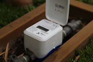 A digital ultrasonic water meter with an open lid installed in an outdoor underground utility box.