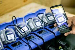 A person uses a smartphone to scan a QR code on a row of blue Laager IoT smart water meters.
