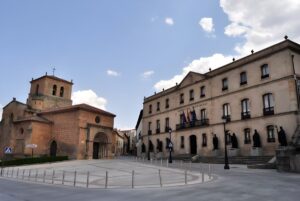 The Provincial Council of Soria building and the Church of San Juan de Rabanera in a paved plaza under a blue sky.