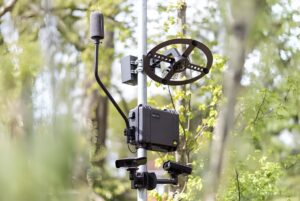 A Soundvue noise detection system with cameras, microphone, and acoustic sensor mounted on a pole in a wooded area.