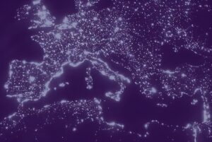 Satellite view of Europe at night with illuminated city lights and urban centers against a purple-toned background.