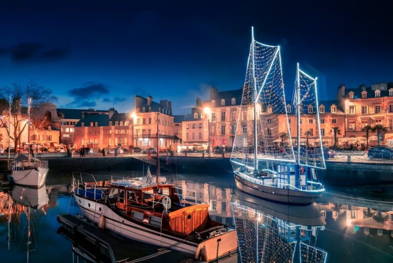 Illuminated boats docked at the Port of Vannes at night with glowing street lights and historic buildings in the background.