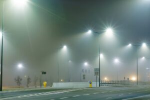 LED street lights illuminating an empty asphalt road and concrete barriers on a foggy night.
