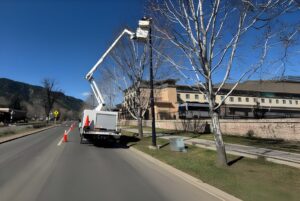 Technician in a CLI Services bucket truck repairing a street lamp on a sunny roadside in Boulder.