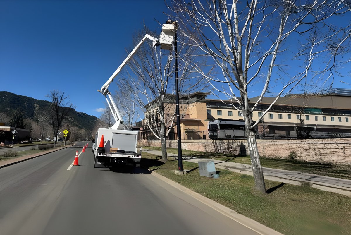 Technician in a CLI Services bucket truck repairing a street lamp on a sunny roadside in Boulder.