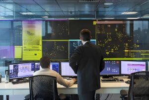 Two operators monitor utility data on a large video wall and desktop screens inside a SUEZ smart operations centre.