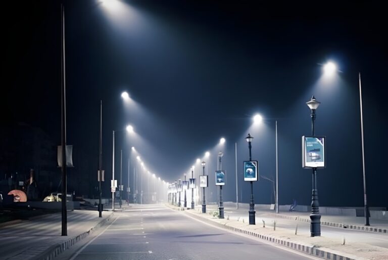 Row of illuminated LED street lamps with attached banners lining an empty urban road at night.