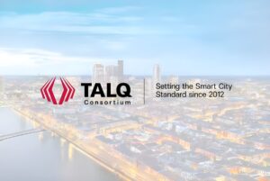TALQ Consortium logo and slogan overlaid on a blurred aerial view of a city skyline at dusk with illuminated streets.