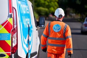 A Thames Water technician in high-visibility clothing walks past a branded utility van on a residential street.