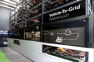 Industrial battery storage racks with Vehicle-To-Grid Feldversuch signage and energy flow diagrams.