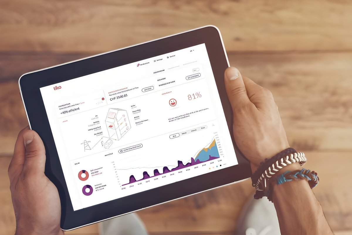 A person holding a tablet displaying the Tiko energy management dashboard with consumption graphs and data.