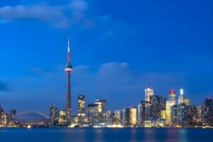 Toronto skyline at dusk featuring the CN Tower and illuminated skyscrapers reflecting on the water.