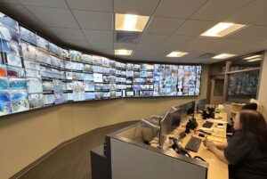 Operators at desks in a traffic management center facing a large curved wall of monitors displaying live road camera feeds.