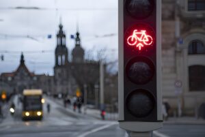 Red bicycle traffic signal illuminated on a city street with a tram and historic architecture in the blurred background.