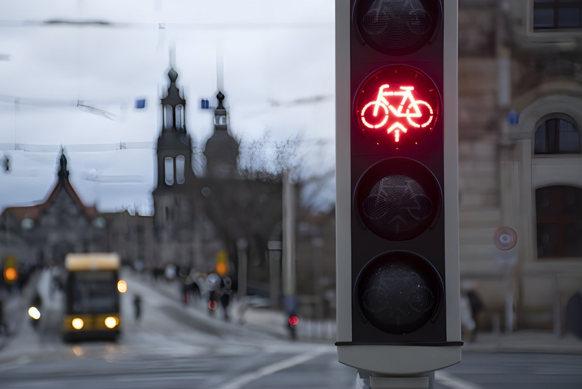 Red bicycle traffic signal illuminated on a city street with a tram and historic architecture in the blurred background.