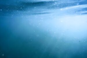 Underwater view of sunlight filtering through blue ocean water with visible bubbles and particles.