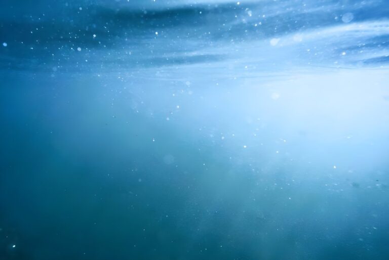 Underwater view of sunlight filtering through blue ocean water with visible bubbles and particles.
