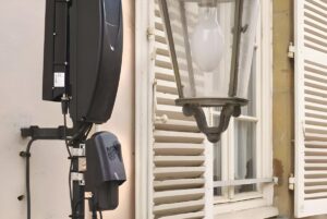 An Upciti smart city sensor and communication module mounted on a wall next to a traditional street lamp and window.