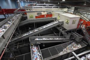 Automated conveyor belts transporting plastic waste and recyclables through a large industrial sorting facility.
