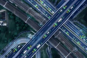 Aerial view of a multi-level highway interchange with digital data overlays and green icons tracking moving vehicles.