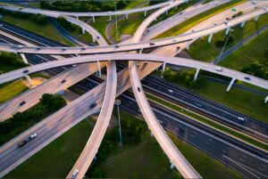 Aerial view of a multi-level highway interchange with cars traveling on curving overpasses and ramps at sunset.