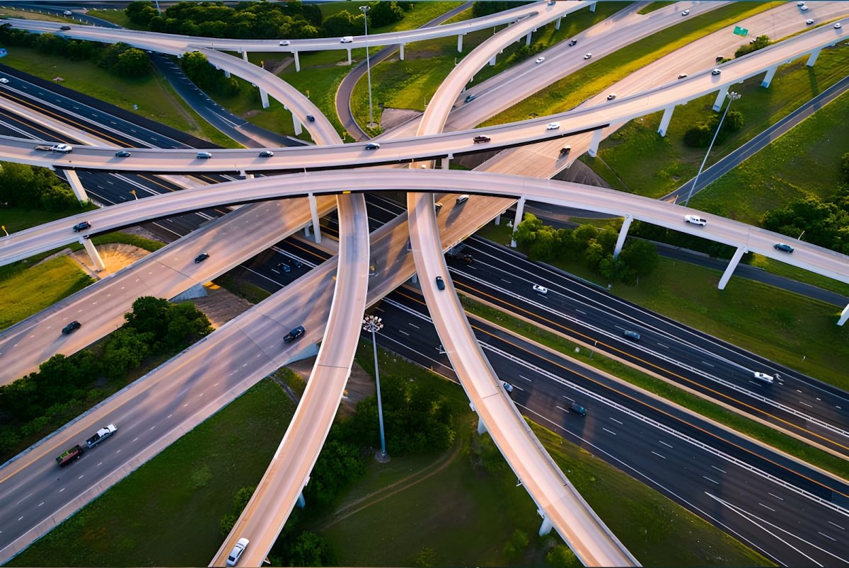 Aerial view of a multi-level highway interchange with cars traveling on curving overpasses and ramps at sunset.