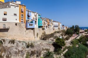 Colorful multi-story houses built atop a stone retaining wall in the coastal town of Villajoyosa, Spain.