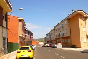 Residential street in Villaquilambre with multi-story brick buildings, parked cars, and overhead street lighting.