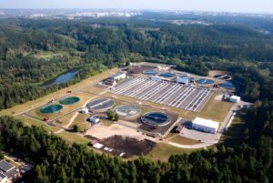 Aerial view of a water treatment plant with circular clarifiers and rectangular aeration tanks surrounded by forest.