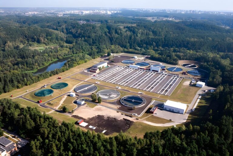 Aerial view of a water treatment plant with circular clarifiers and rectangular aeration tanks surrounded by forest.