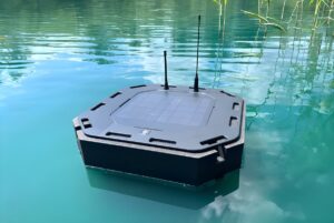 A WATR solar-powered water quality monitoring buoy with two antennas floating on a calm turquoise lake.