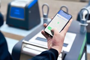 A person uses a smartphone app to unlock a Waste Vision smart waste container on a city sidewalk.
