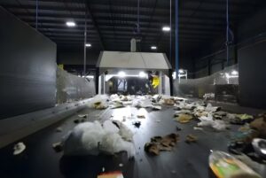 An AMP Robotics automated sorting system processes waste on a conveyor belt inside a recycling facility.