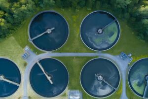 Aerial top-down view of circular wastewater treatment clarifier tanks surrounded by green grass and trees.