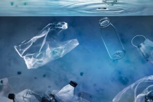 Plastic bottles, a grocery bag, and a face mask floating underwater in blue ocean water.